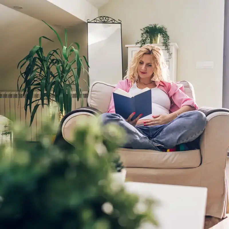 Donna incinta legge un libro in una stanza con piante