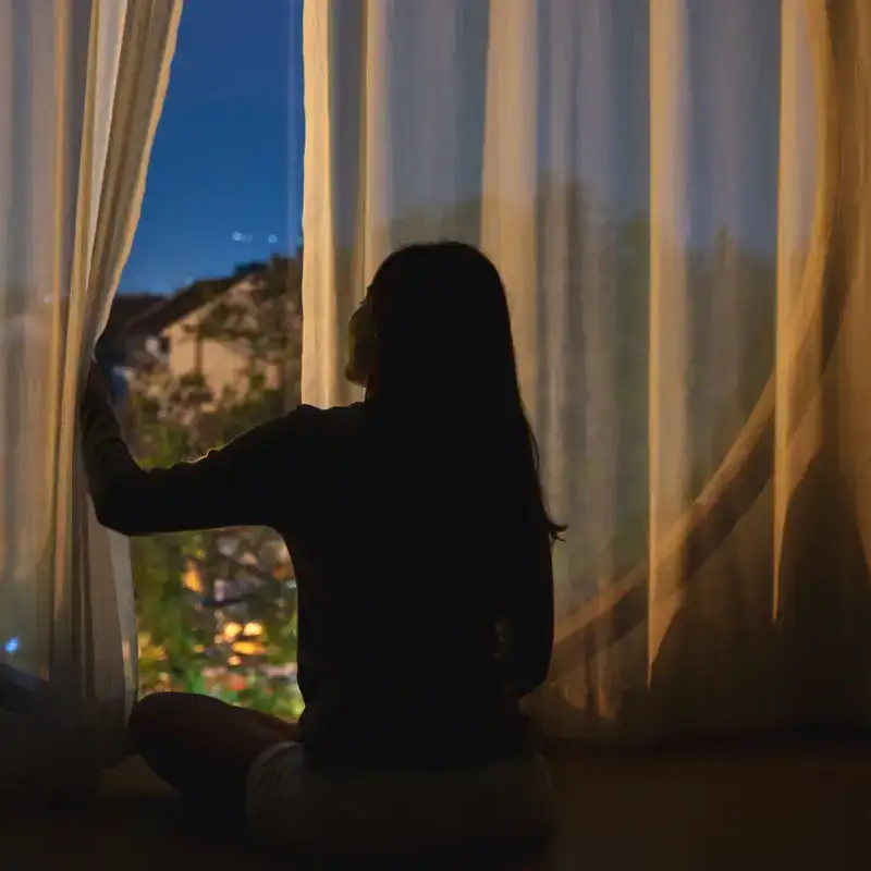 Donna che guarda fuori dalla finestra con tenda aperta