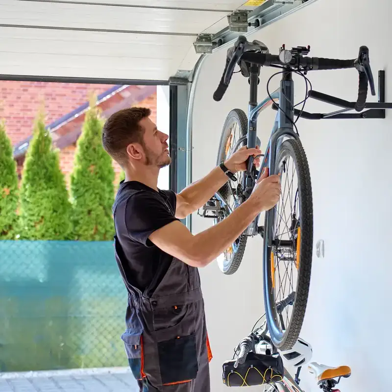 Uomo sistema una bicicletta appesa al muro del garage