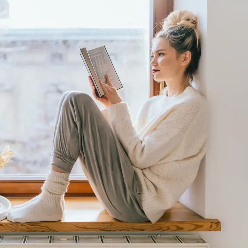 Donna che legge un libro vicino alla finestra