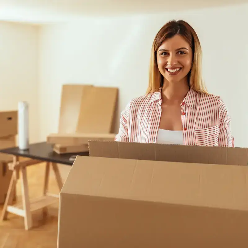 Donna sorridente con scatola di cartone in una stanza minimalista